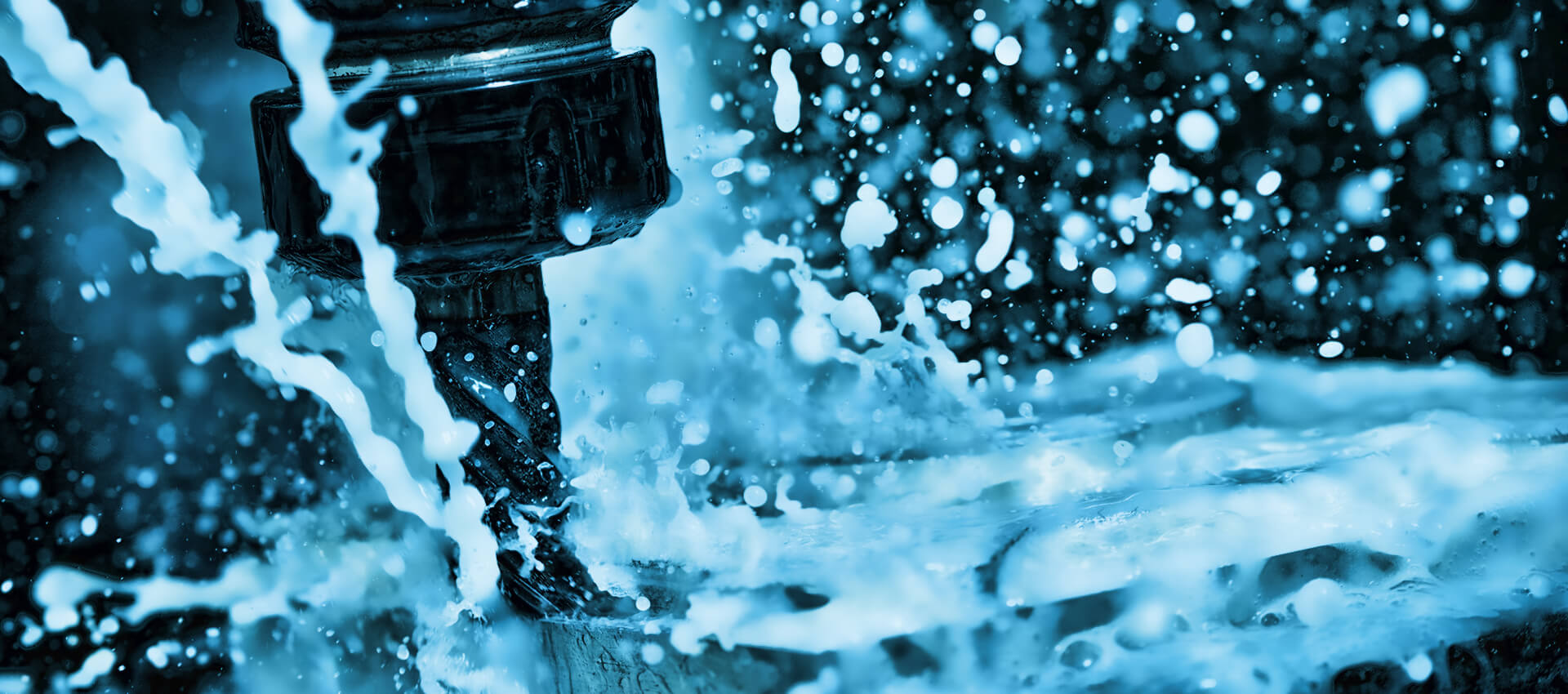 CNC machine drill bit surrounded by splashing coolant fluid